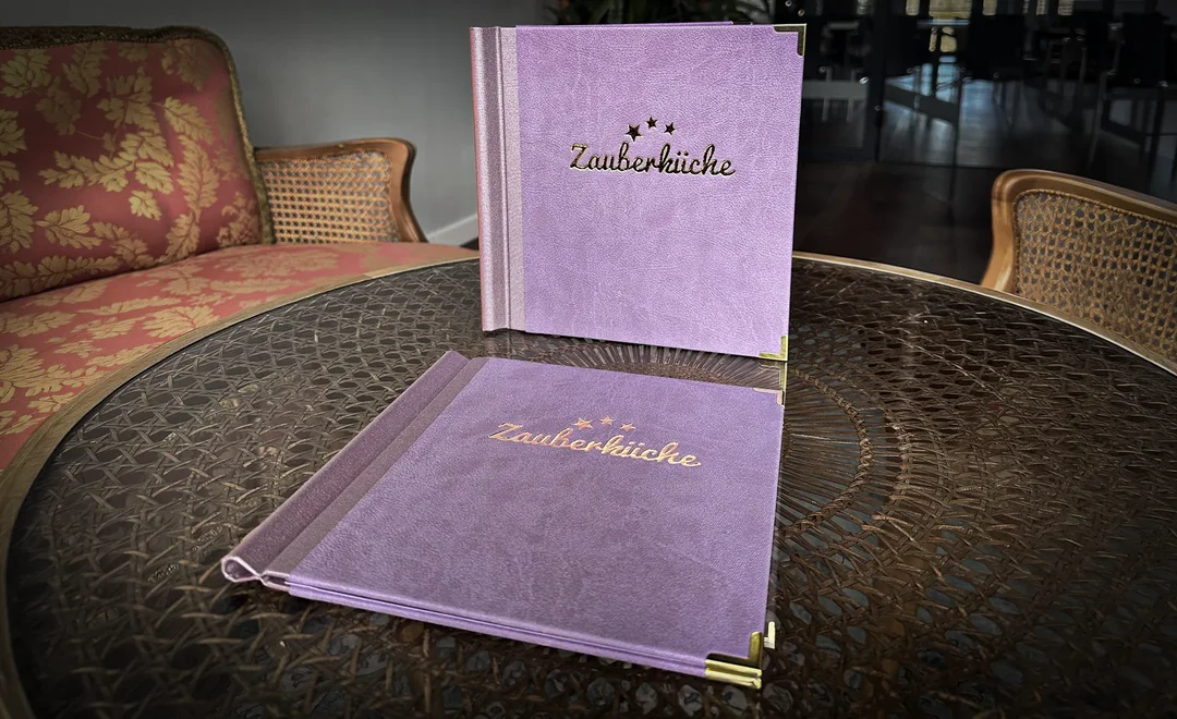 Menue-Buch der Zauberküche, fotografiert auf einem Glastisch.